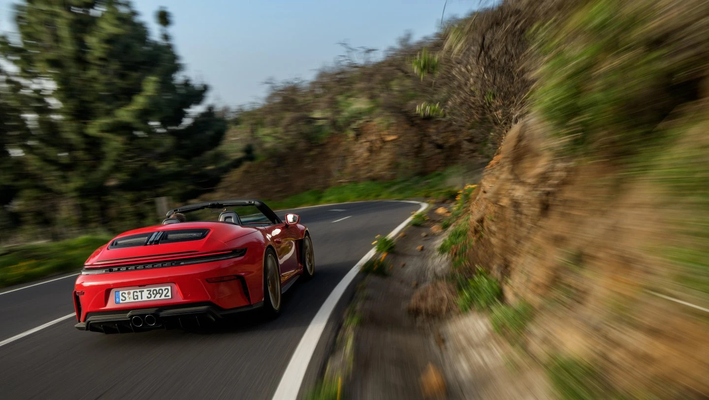 Rear view of a red 2026 Porsche 911 GT3 S/C driving through a winding mountain road.
