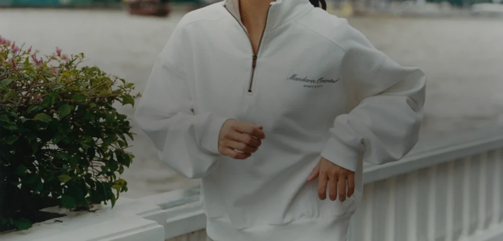 A model wearing the Mandarin Oriental Bangkok x Sporty & Rich 150th-anniversary capsule in a hotel setting.