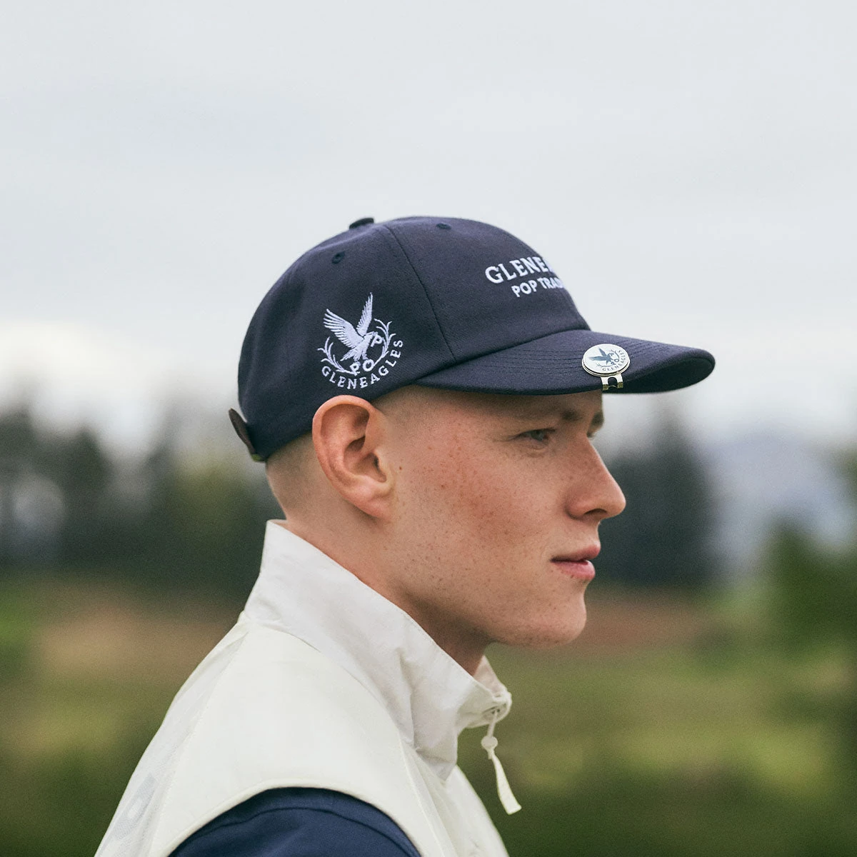 Model wearing the navy Pop Trading Company x Gleneagles wool six-panel cap outdoors.
