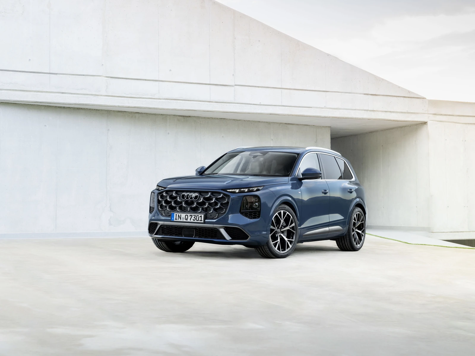 Blue Audi Q7 SUV shown from the front three-quarter angle against a light architectural background.