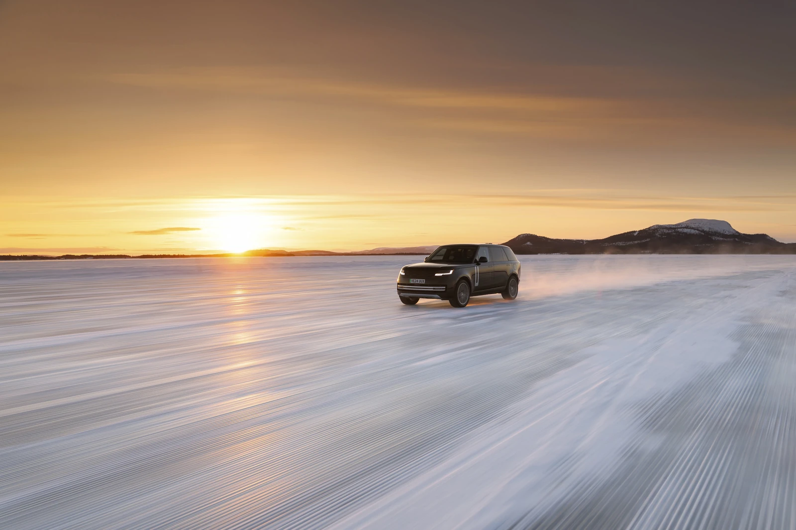 Range Rover Electric driving across a snowy test landscape at sunset.