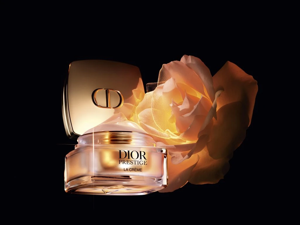 Open jar of Dior Prestige La Crème beside its gold lid and a rose on a dark background.