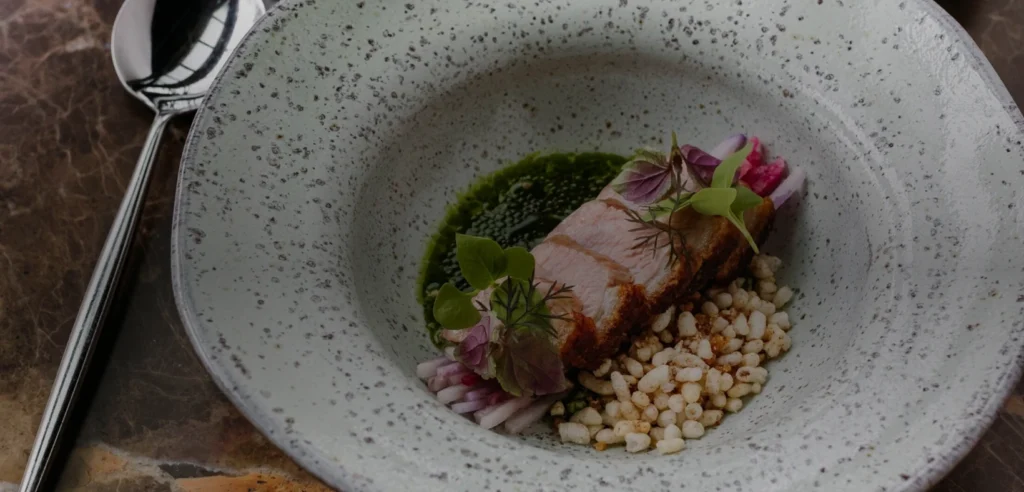 An AnnaLena tasting-menu dish with seared fish, green herb sauce, puffed grains, microgreens and edible flowers.