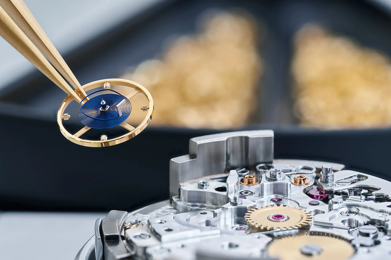 Rolex movement assembly with a blue Parachrom hairspring and gold Microstella balance held above the movement.
