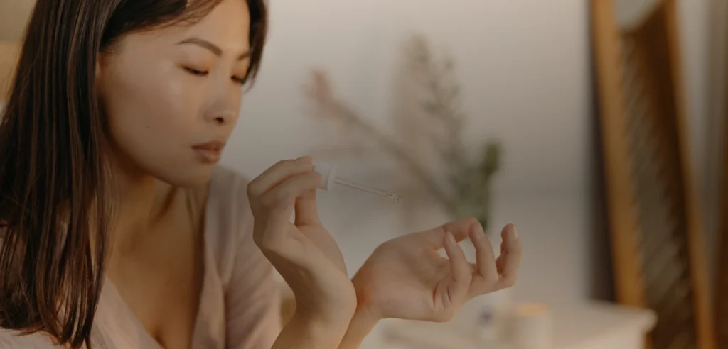 Woman holding a glass skincare serum dropper near her hand